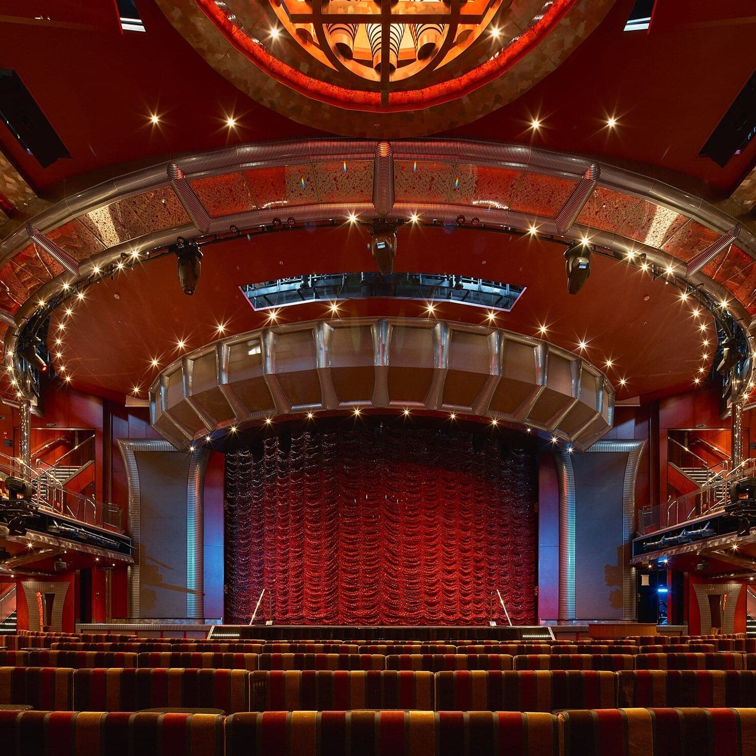 El teatro del Costa Fascinosa, con las butacas rayadas, el escenario con telón rojo y la cúpula iluminada