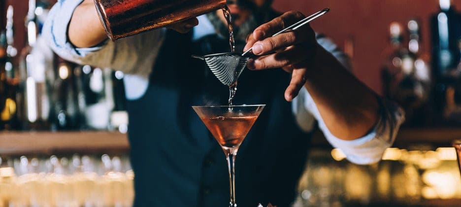 Un barman sirve un cóctel a través de un colador en una copa, en un bar del Costa Serena