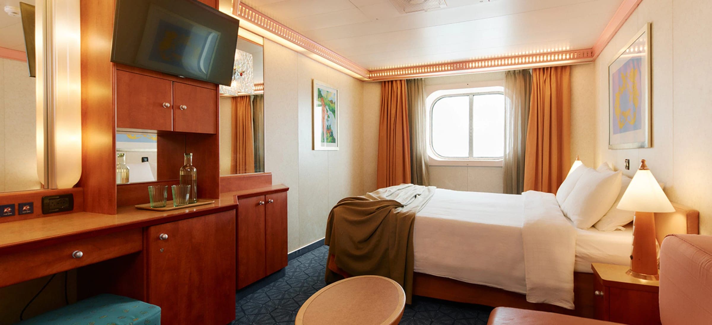 Cabina externa del Costa Serena: cama matrimonial, escritorio con televisor y una ventana redonda al mar