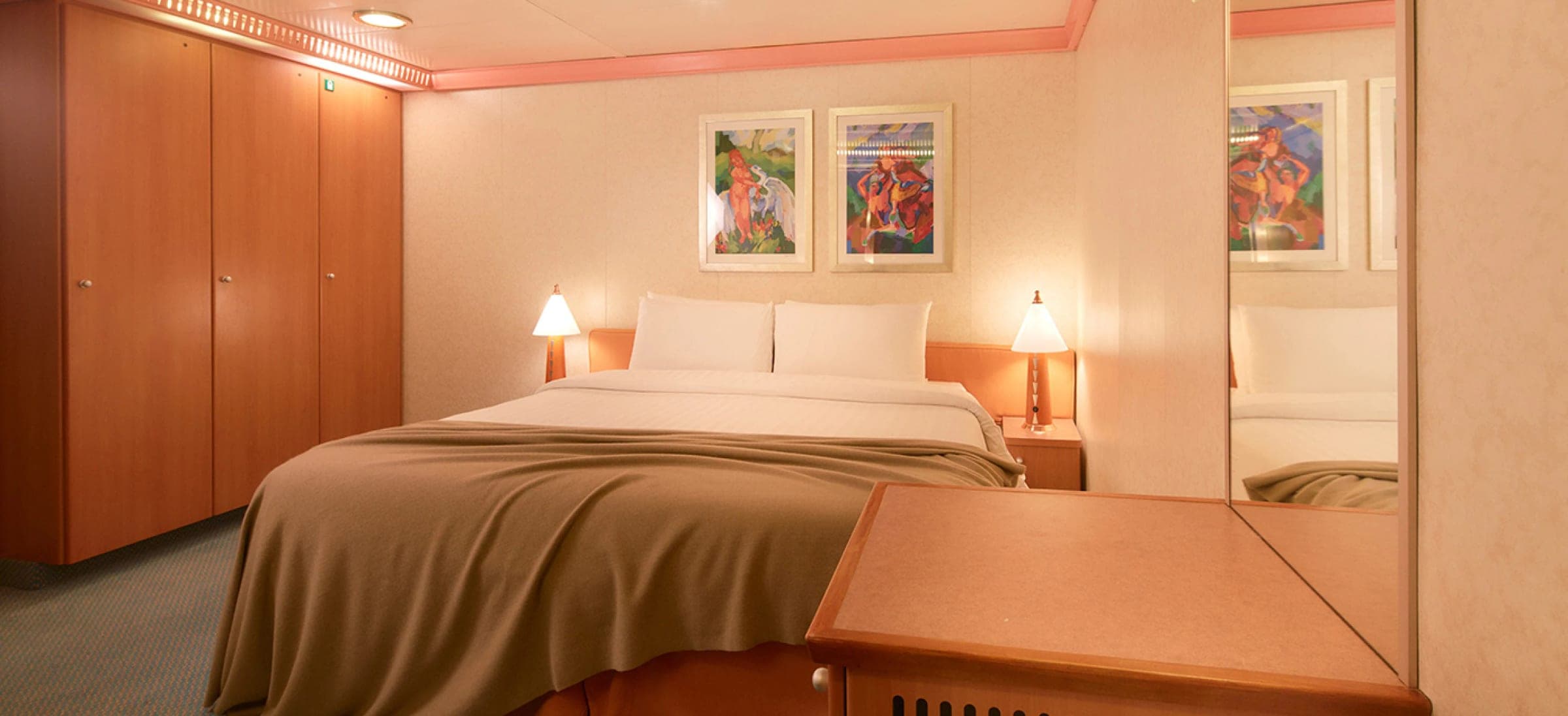 Cabina interna del Costa Serena: cama matrimonial con manta, dos veladores, cuadros y placard, sin ventana