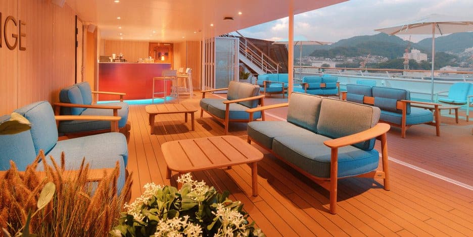 Cubierta del Costa Serena con bar, sillones y pileta, frente a una costa con cerros