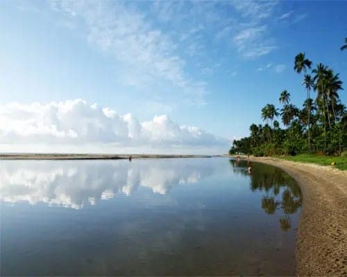 Una laguna quieta de Maragogi que refleja las nubes, con palmeras en la orilla