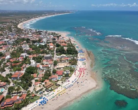 Vista aérea de Porto de Galinhas: el pueblo, la playa con sombrillas y el arrecife que dibuja las piscinas naturales en el mar