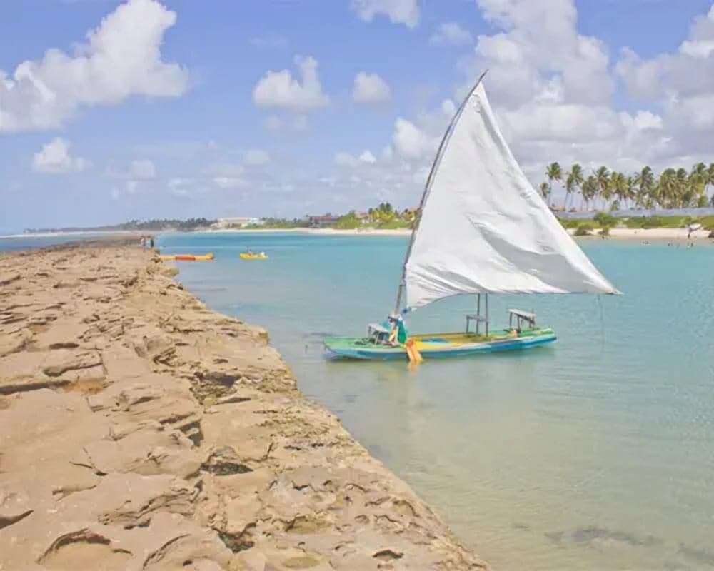 Una jangada de vela blanca amarrada junto al borde del arrecife en Porto de Galinhas, con la playa y las palmeras al fondo