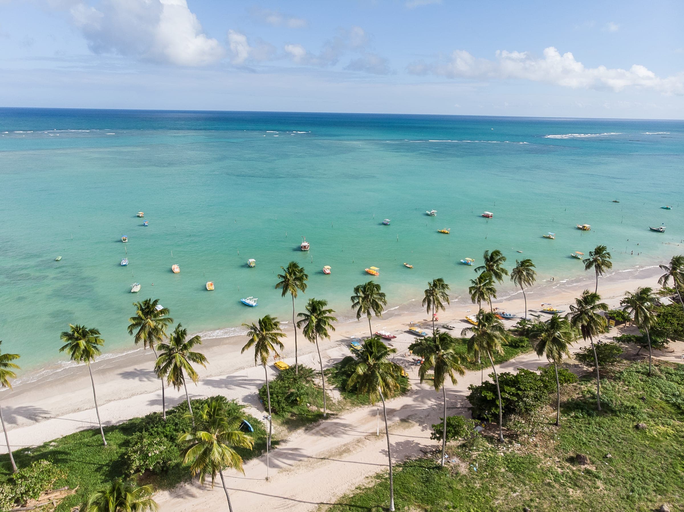 Playa de São Miguel dos Milagres, en Alagoas, con cocoteros y barcos de pesca en la laguna