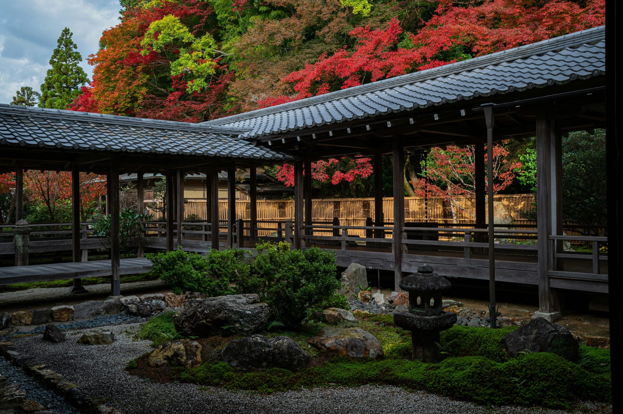 Corredor cubierto de madera y jardín de grava con una linterna de piedra en un templo de Japón, con arces rojos de otoño