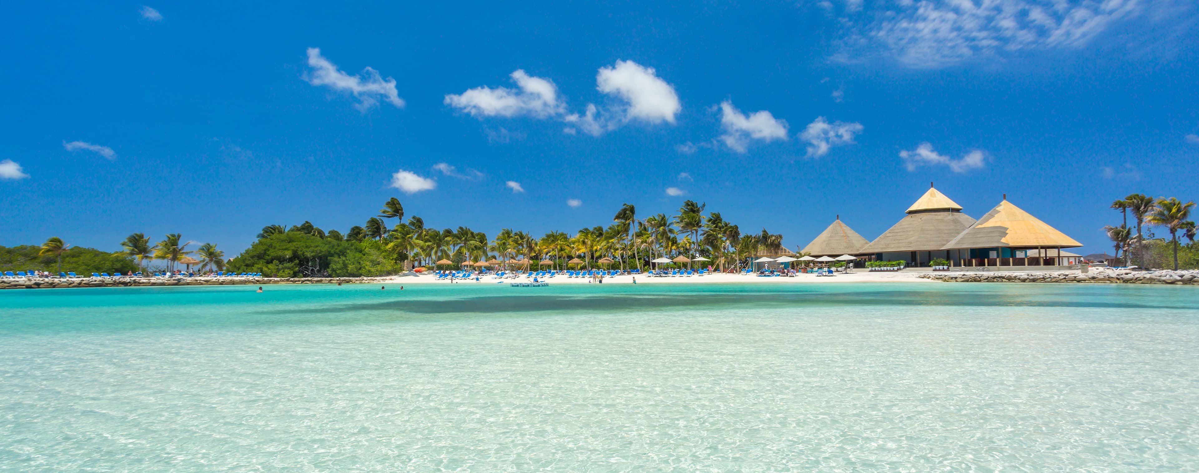 Playa de arena blanca con palmeras, sombrillas de paja y agua turquesa en Aruba