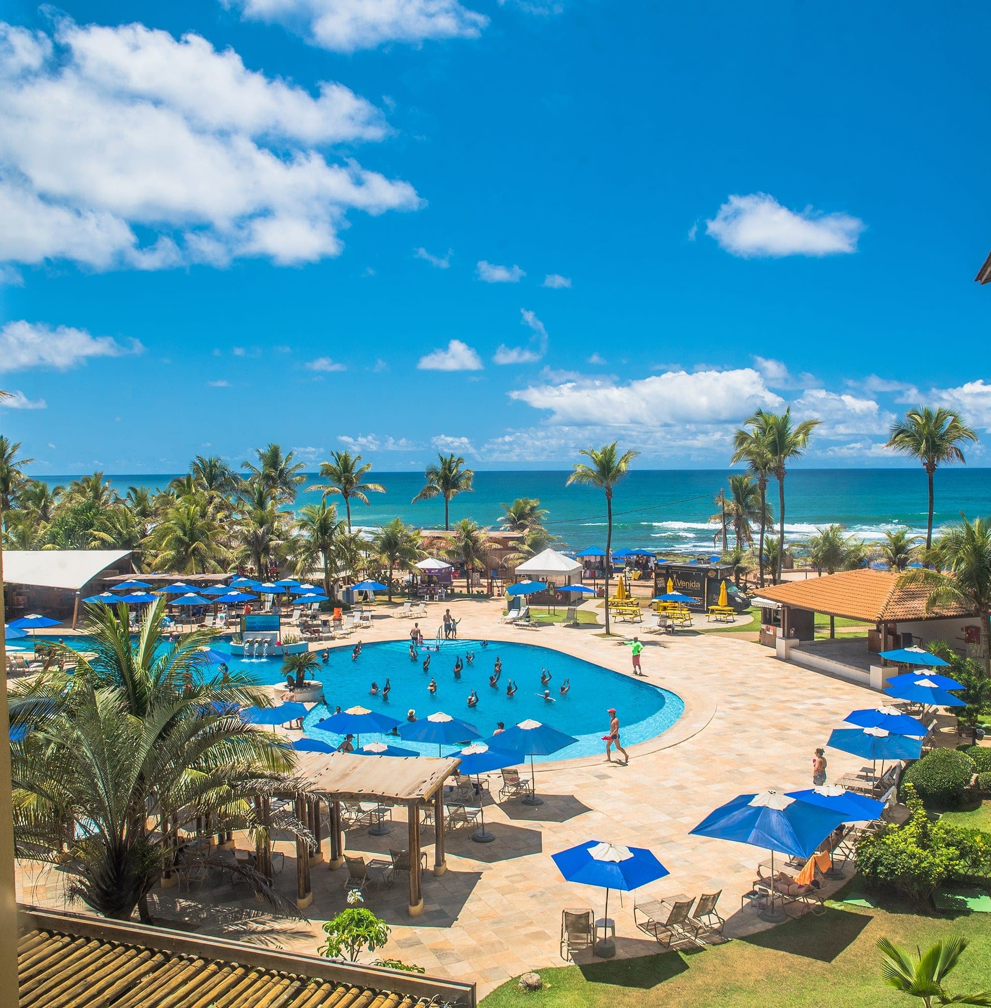 La pileta del hotel rodeada de sombrillas azules y palmeras, con el mar detrás