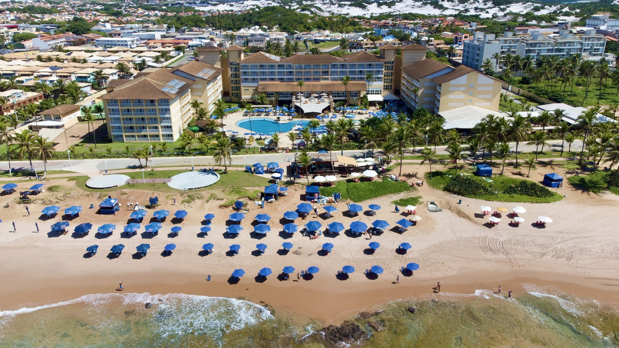 Vista aérea del hotel, la costanera y la playa de Stella Maris, con sombrillas azules sobre la arena y el mar delante