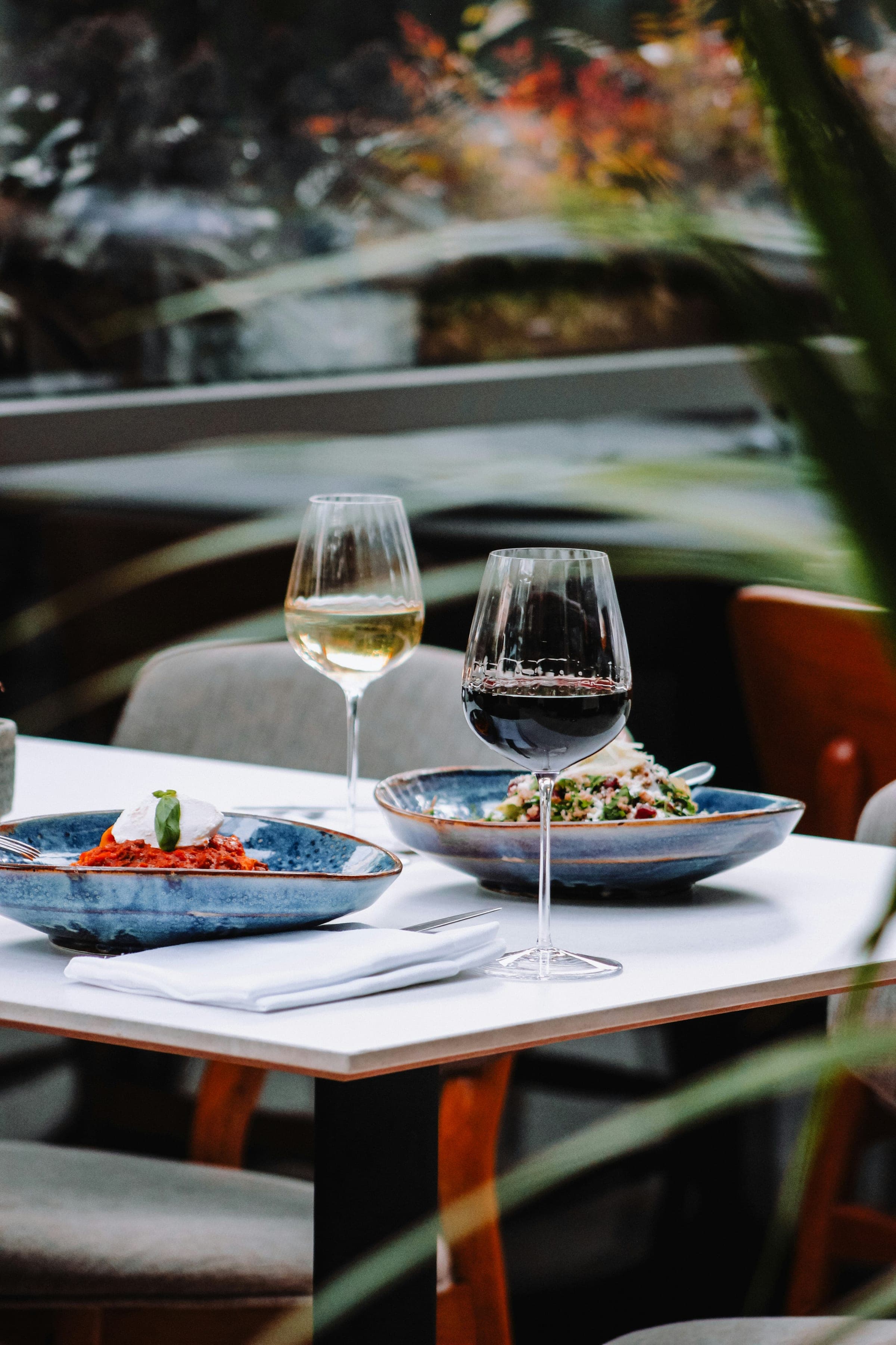 Mesa de restaurante con dos platos hondos de cerámica azul, una copa de vino blanco y una de tinto, y una servilleta de tela blanca