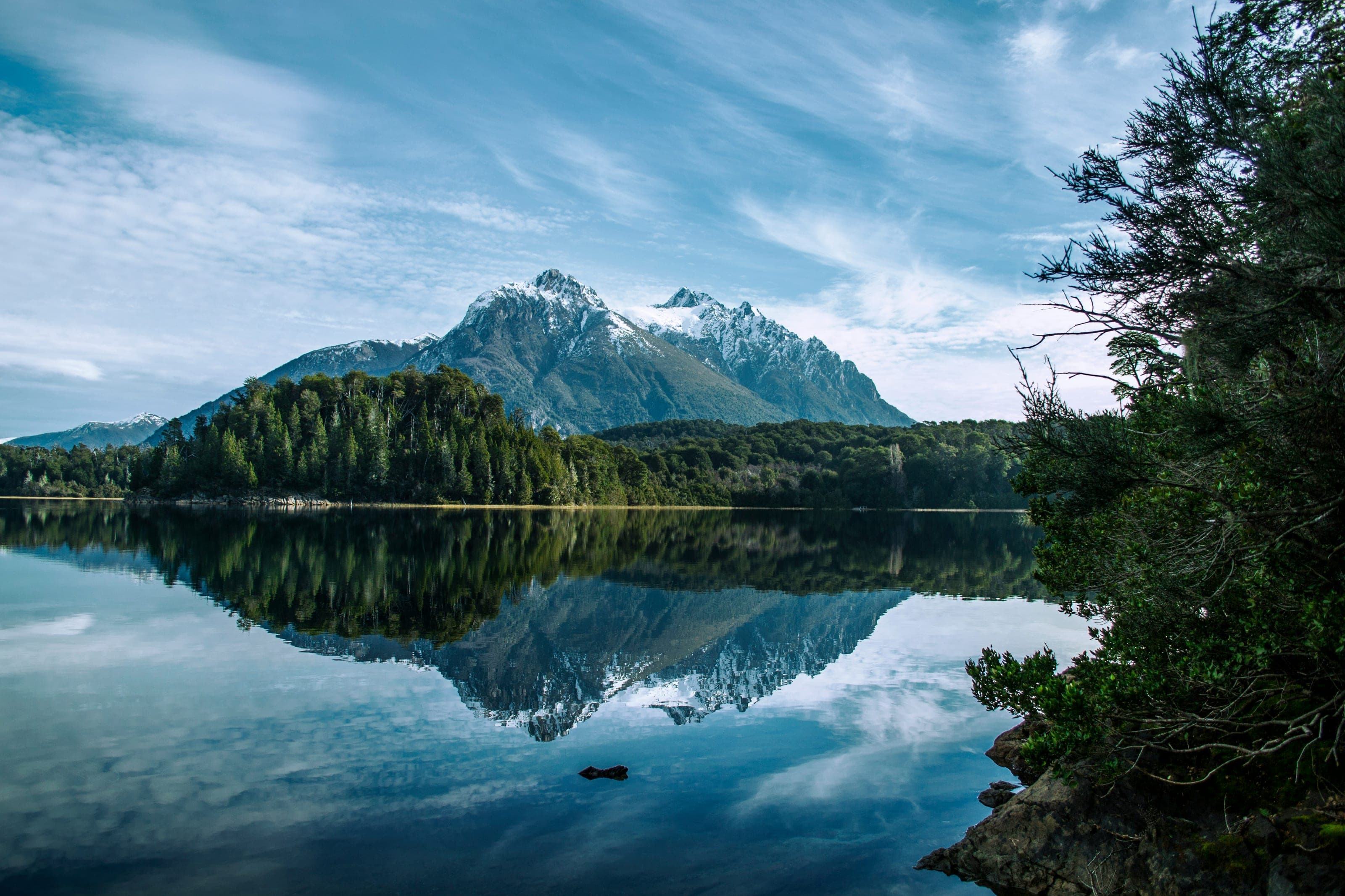Lago en calma que refleja un cerro nevado y el bosque de la orilla, en Bariloche