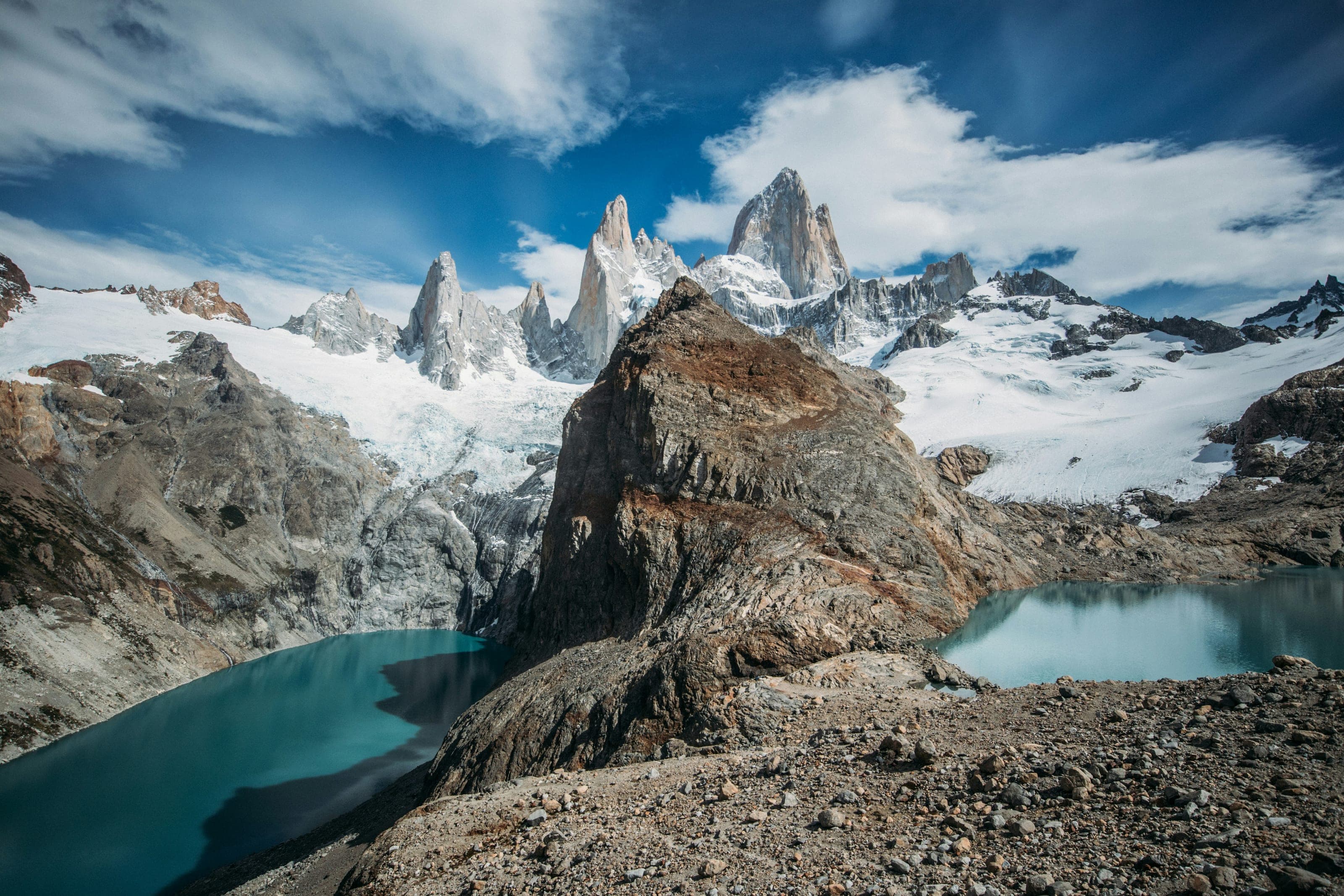 Agujas de granito del Fitz Roy con nieve sobre dos lagunas, una turquesa y otra celeste, separadas por un morro de roca